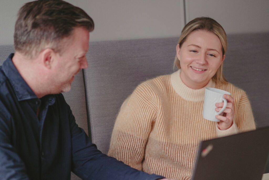 Mann og dame i samtale foran PC-skjermen. Hun holder en kaffekopp.